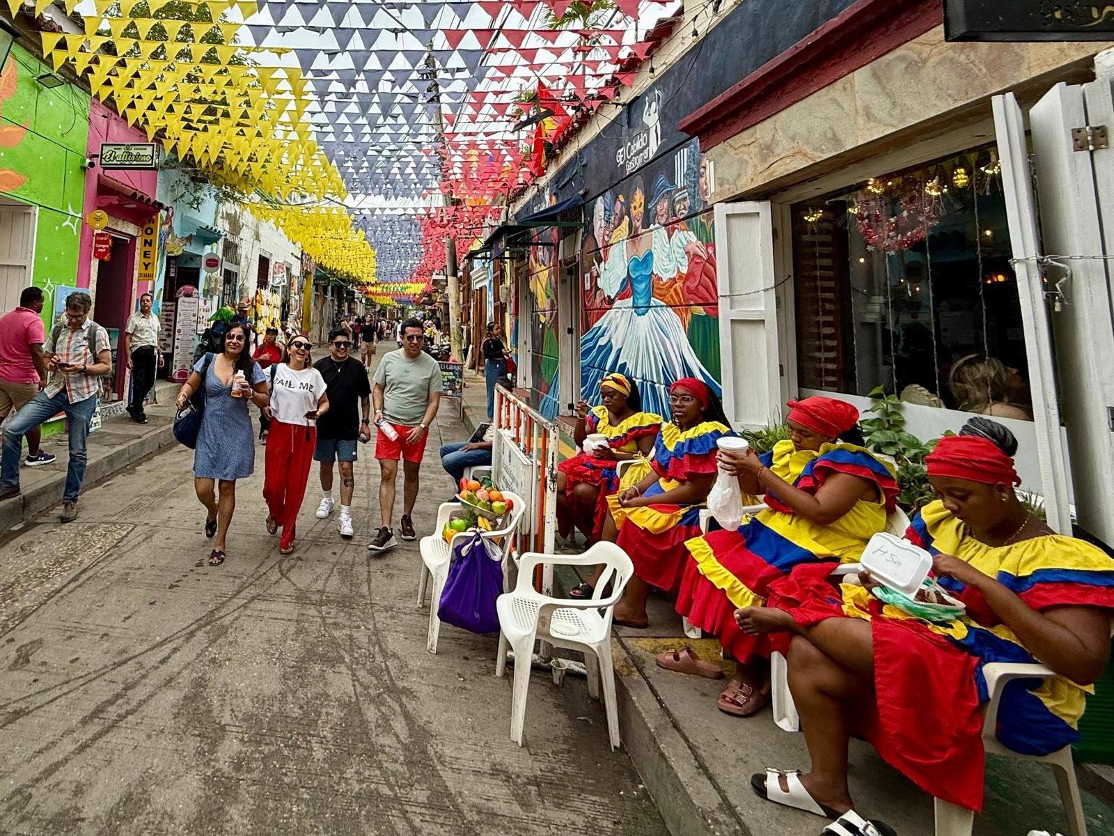 Personalised travel planning for your trip to Colombia — Palenqueras in traditional red, yellow, and blue dresses on a vibrant bunting-lined street in Cartagena